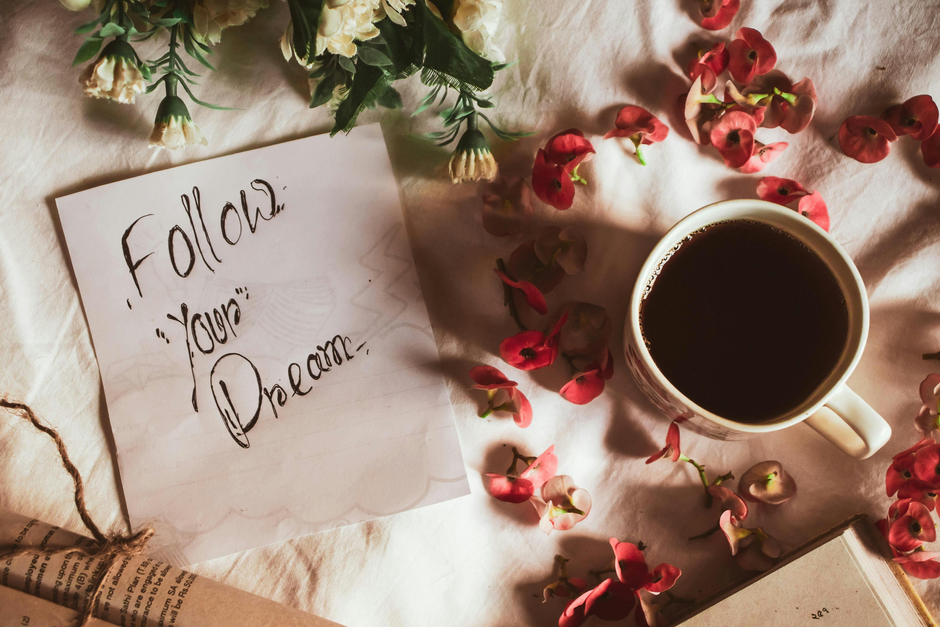A flat lay of note paper with the handwritten words 'follow your dream' with a cup of coffee and flowers