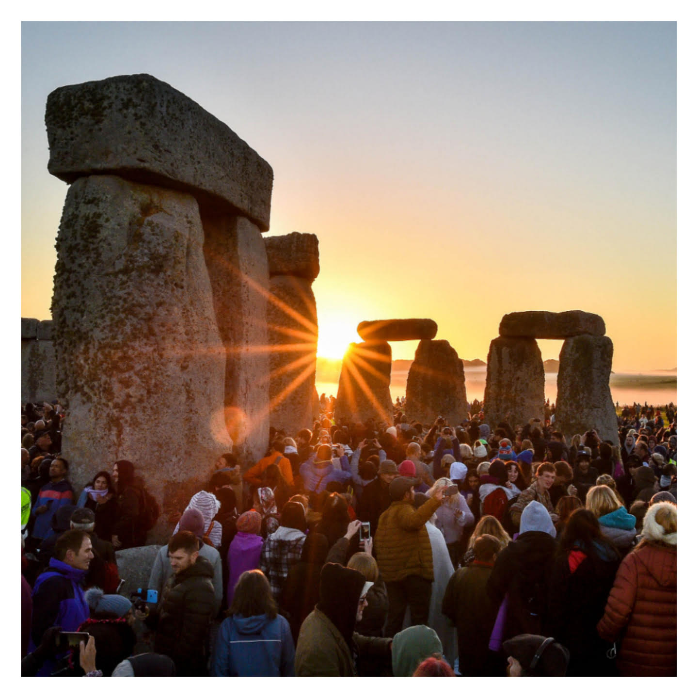 A crowd watches as the sunrise shines through Stonehenge